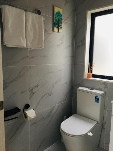 a white bathroom with a toilet and a window at West Auckland Delight Stay in Auckland