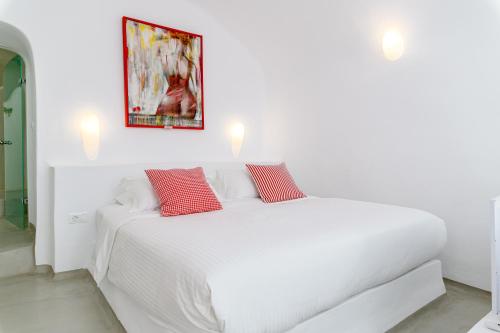 a white bed with two red pillows on it at Trieris Villa & Suites in Fira