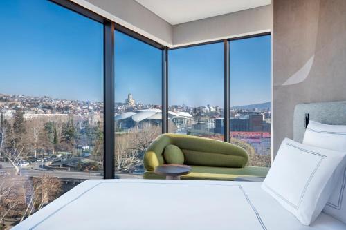 a bedroom with a green chair and large windows at Swissôtel Tbilisi in Tbilisi City