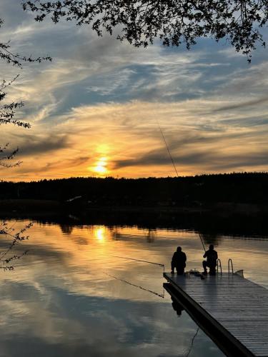 two people sitting on a dock fishing on a lake at Chce się być in Ślesin