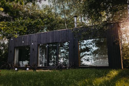 a black house with large windows in the grass at Ezernams SPA in Kaukuri