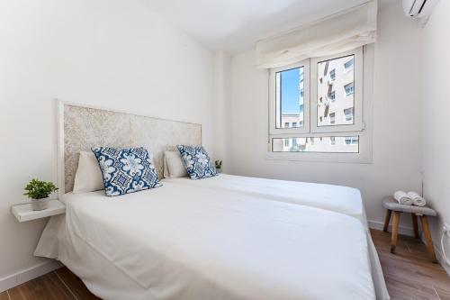- une chambre blanche avec un grand lit blanc et des oreillers bleus dans l'établissement MalagaSuite Malagueta Beach & Sun, à Malaga