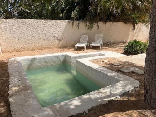 a pool of water with two chairs next to a palm tree at Résidence 360 in Mezraya