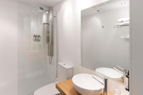 a white bathroom with two sinks and a shower at Petit Palace Tres Cruces in Madrid