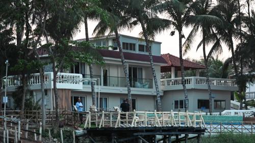 a white house with palm trees in front of it at Damodar River Retreat, Uluberia in Uluberiya