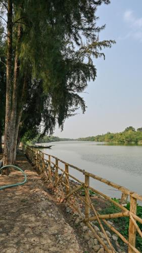 a wooden fence next to a body of water at Damodar River Retreat, Uluberia in Uluberiya