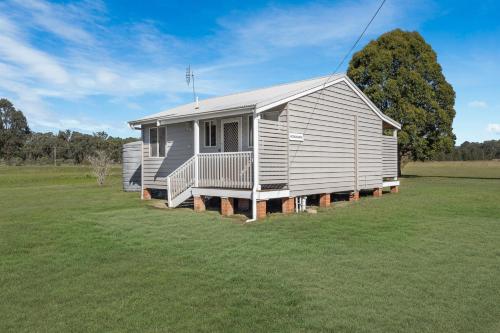 a small white house in a grassy field at Madigan Cottages - The Kookaburra Cottage in Lovedale