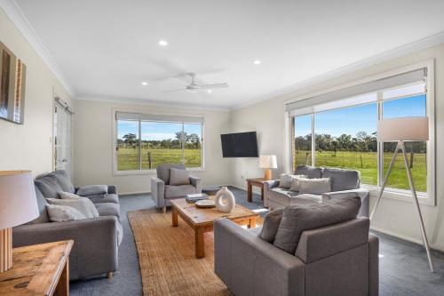 a living room with couches and a tv and windows at Madigan Cottages - The Homestead in Lovedale
