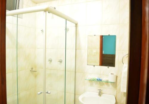 uma casa de banho com um chuveiro, um lavatório e um espelho. em Hotel Faenician em Aparecida