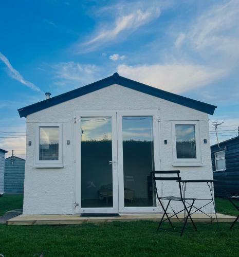 a white house with two chairs in the grass at The Cosy Summer House in Leysdown-on-Sea