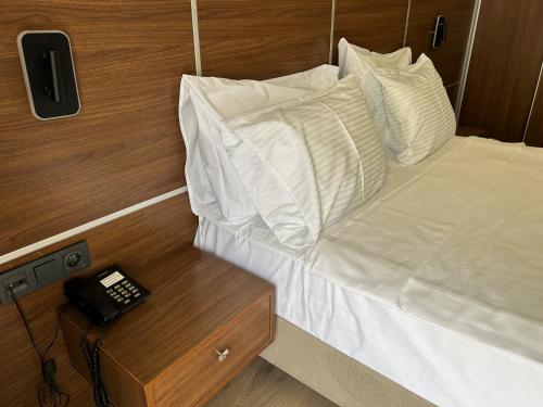 a bed with white sheets and a phone on a table at Gulluk Life Hotel in Gulluk