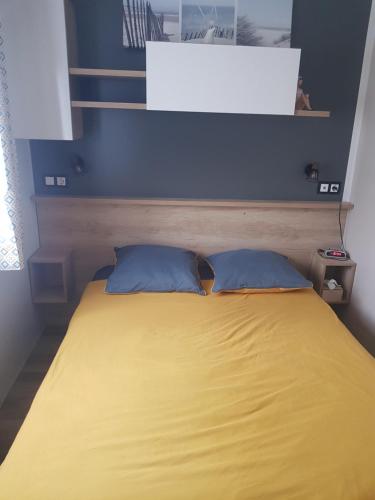 a yellow bed with two blue pillows in a room at les dunes de contis in Saint-Julien-en-Born