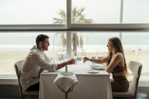 a man and woman sitting at a table with wine glasses at Cádiz Bahía by QHotels in Cádiz