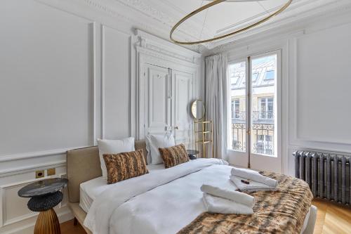- une chambre blanche avec un grand lit et une grande fenêtre dans l'établissement Sublime Apartment Montaigne Arc de Triomphe by Studioprestige, à Paris