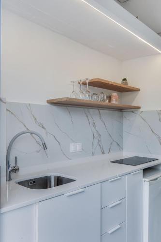 a white kitchen with a sink and a shelf at Veneto Sea View Apartments in Stalida