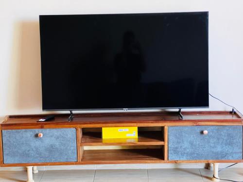 telewizor z płaskim ekranem siedzący na szczycie drewnianego centrum rozrywki w obiekcie The home hive apartment w mieście Kampala