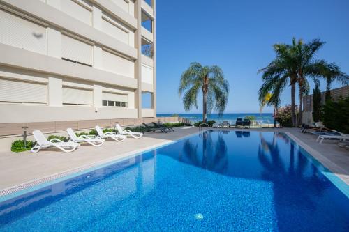 a swimming pool with chairs and the ocean in the background at Hallmark Beach by TrulyCyprus in Limassol