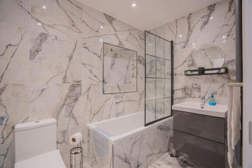 a bathroom with a white tub and a marble wall at Spacious 3BR Home by D3 Short Stay, Sleep 9, Free WIFI & Parking in London
