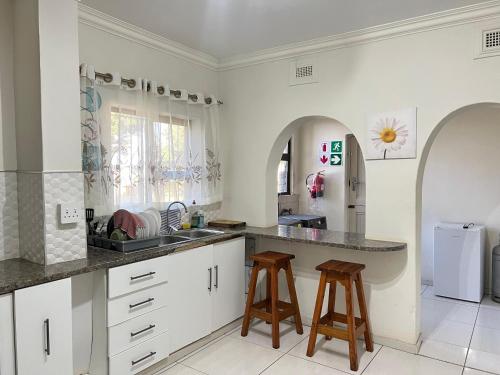 a kitchen with white cabinets and a sink and stools at La Vue in Port Shepstone