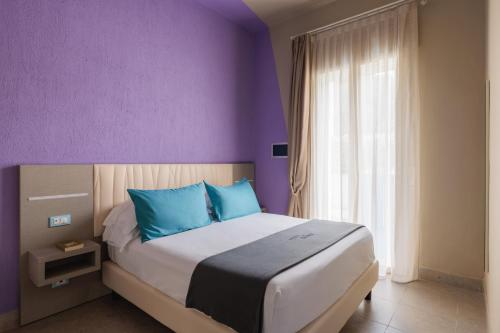 a bedroom with purple walls and a bed with blue pillows at Hotel Nina in Marina di Bibbona