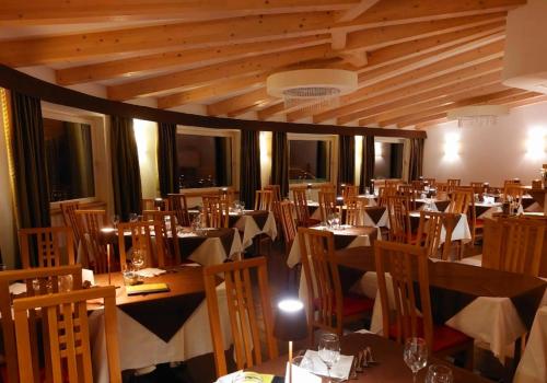 a dining room with tables and chairs in a room with wooden ceilings at Ciasa Alpina Relax Hotel in Moena