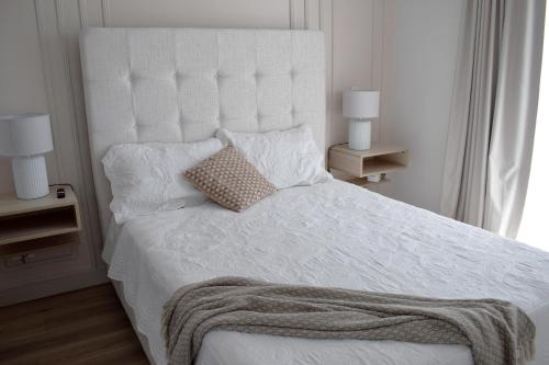 a white bed with a white headboard and two lamps at Apartamento con piscina y espacio de trabajo in San José
