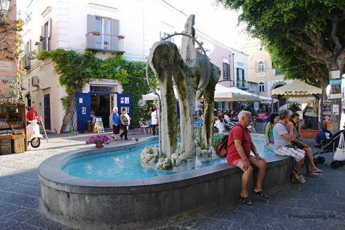 une fontaine dans une rue avec des gens assis autour de celle-ci dans l'établissement Ischia forio monolocale arredato, à Ischia