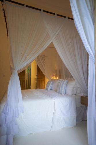 a bedroom with a white bed with white drapes at Santa Fe Casas Hotel Trancoso in Trancoso