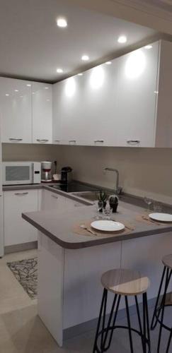 une cuisine avec des armoires blanches et un comptoir avec des tabourets dans l'établissement Le Castille - à deux pas des plages, à Cannes