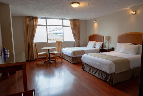 Habitación de hotel con 2 camas, mesa y ventana en Hotel Santa Monica, en Cuenca