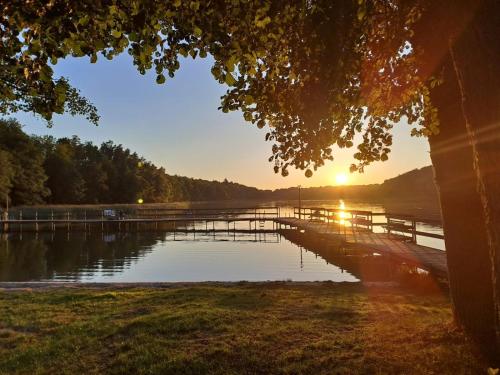 a dock on a lake with the sun setting at Domki nad jeziorem in Przechlewo