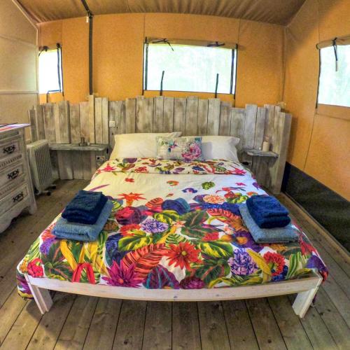 une chambre avec un grand lit avec une couverture colorée dans l'établissement Luxury Safari Tent with Hot Tub at Camping La Fortinerie, à Mouliherne