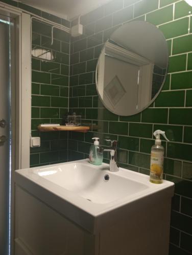 uma casa de banho com azulejos verdes, um lavatório e um espelho. em Ackes Stuga 32 em Örebro