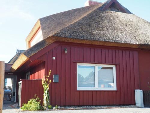 un edificio rojo con techo de paja y ventana en Dwargenhus, en Prerow