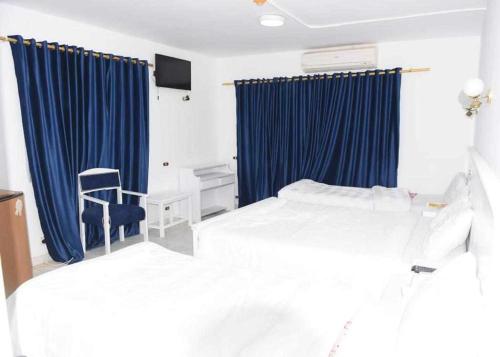 a bedroom with two beds with blue curtains and a chair at El Kasr Hotel in Marsa Matruh