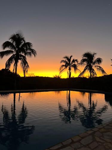 a sunset with palm trees in front of a pool at Complexo Luquinha in Iacaiá