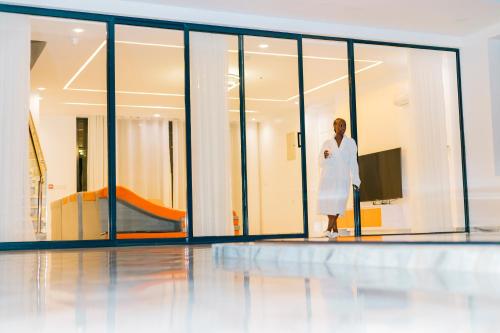 a woman in a white dress standing in a room with windows at B&P Ever Retreat Villa Gisenyi in Gisenyi