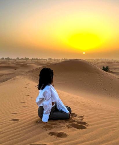 a woman sitting in the desert watching the sunset at Holiday Desert Camp in Merzouga