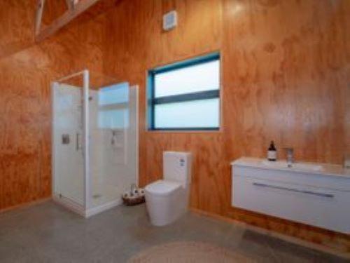 a bathroom with a toilet and a sink and a window at Hosts on the Coast Family fun in Whiritoa in Whiritoa