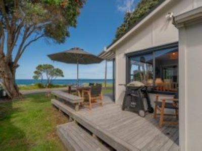 a porch with a picnic table and an umbrella at Hosts on the Coast Family fun in Whiritoa in Whiritoa