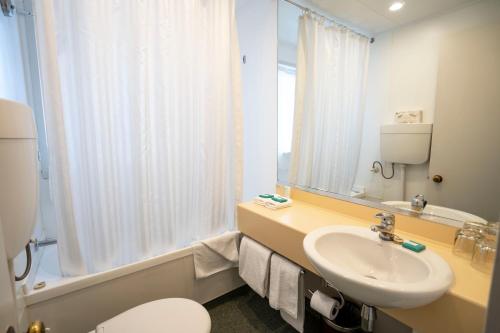 Heartland Hotel Queenstown في كوينزتاون: حمام مع حوض ومرحاض ومرآة