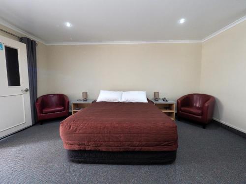 a hotel room with a bed and two chairs at Ulster Lodge Motel in Hamilton