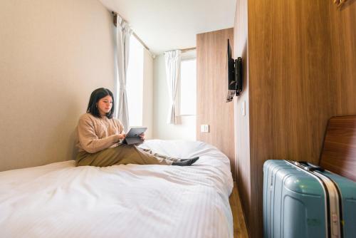 une femme assise sur un lit utilisant un ordinateur portable dans l'établissement &AND HOSTEL ASAKUSA KAPPABASHI, à Tokyo