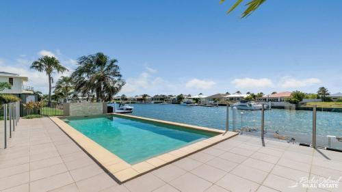 a swimming pool next to a river with boats at Canal Serenity Retreat in Banksia Beach