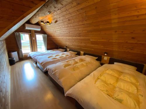 3 camas en una habitación con pared de madera en Cottage Jokigen, en Yamanakako