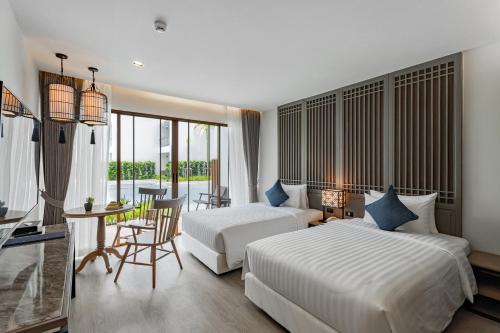 a hotel room with two beds and a table and chairs at Bella Nara Phuket Naiyang Beach in Nai Yang Beach