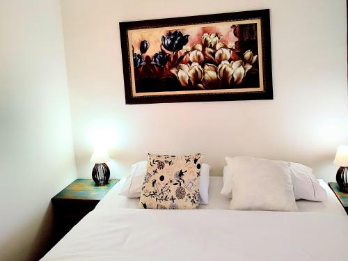 a bedroom with a white bed with a painting on the wall at Pousada Caminhos da Vila Chantal in Campos do Jordão