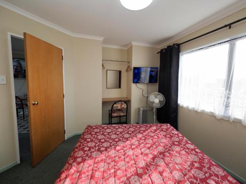 a bedroom with a red bed and a window at Ulster Lodge Motel in Hamilton