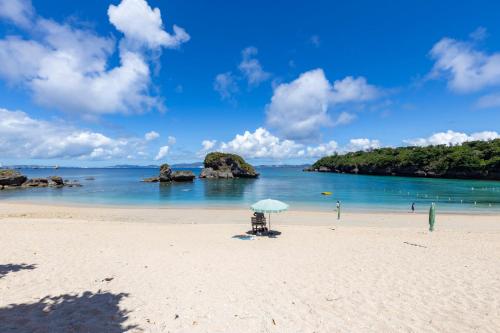 a beach with a chair and an umbrella on the sand at KATSUREN Blue. in Uruma