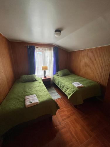 two beds in a room with green sheets and a window at Cabañas Español Coyhaique in Coihaique